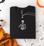 Flat lay of a a black Comfort Colors shirt featuring an embroidered skeleton whisking ingredients in a mixing bowl on a white background 