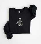Flat lay of a Black Gildan sweatshirt featuring an embroidered skeleton whisking ingredients in a mixing bowl on a white background 
