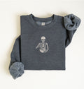 Flat lay of a dark heather gray Gildan sweatshirt featuring an embroidered skeleton whisking ingredients in a mixing bowl on a white background 
