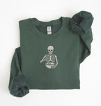 Flat lay of a forest green Gildan sweatshirt featuring an embroidered skeleton whisking ingredients in a mixing bowl on a white background 