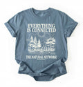 Flat lay of a stone blue t-shirt featuring a forest and fungi illustration with text reading “Everything Is Connected The Natural Network.” perfect gift for nature lovers and eco friendly lifestyle on a white background 