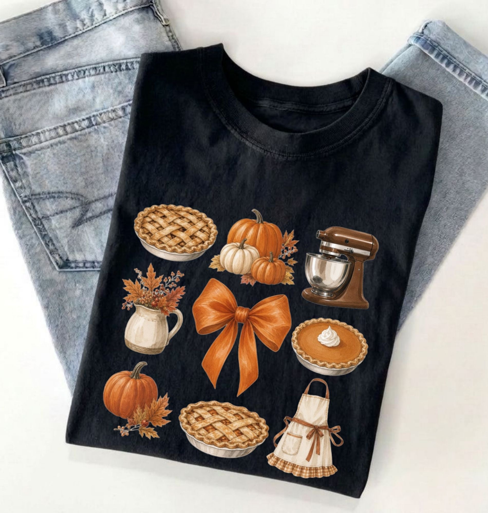 Flat lay of a black fall baking shirt featuring pumpkin pies, pumpkins, autumn leaves, a stand mixer, baking apron and orange bow on a white background 