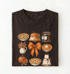 A folded dark chocolate crewneck t-shirt with a graphic print of autumn and fall baking elements, including pies, pumpkins, a stand mixer, a bow, and an apron, on a white background.