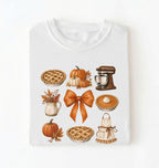 Flat lay of a white fall baking shirt featuring pumpkin pies, pumpkins, autumn leaves, a stand mixer, baking apron and orange bow on a white background 