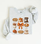 Flat lay of an ash fall baking sweatshirt featuring pumpkin pies, pumpkins, autumn leaves, a stand mixer, baking apron and orange bow on a white background 