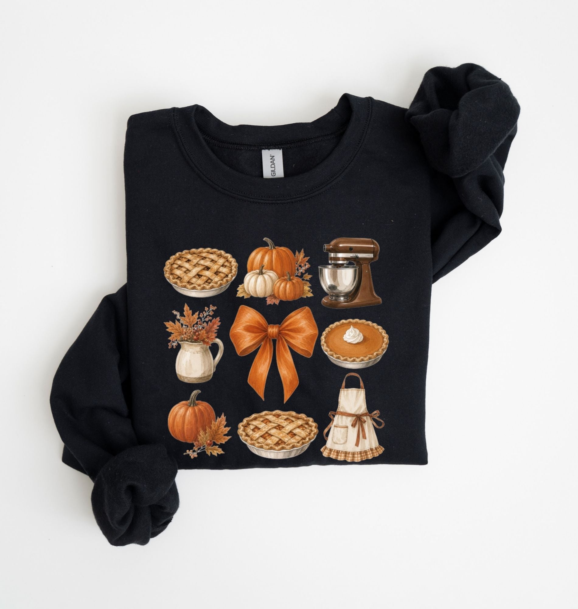 A black crewneck sweatshirt with rolled sleeves, featuring a graphic print of autumn-themed illustrations including pies, pumpkins, a stand mixer, a pitcher of fall leaves, and an apron on a white background.