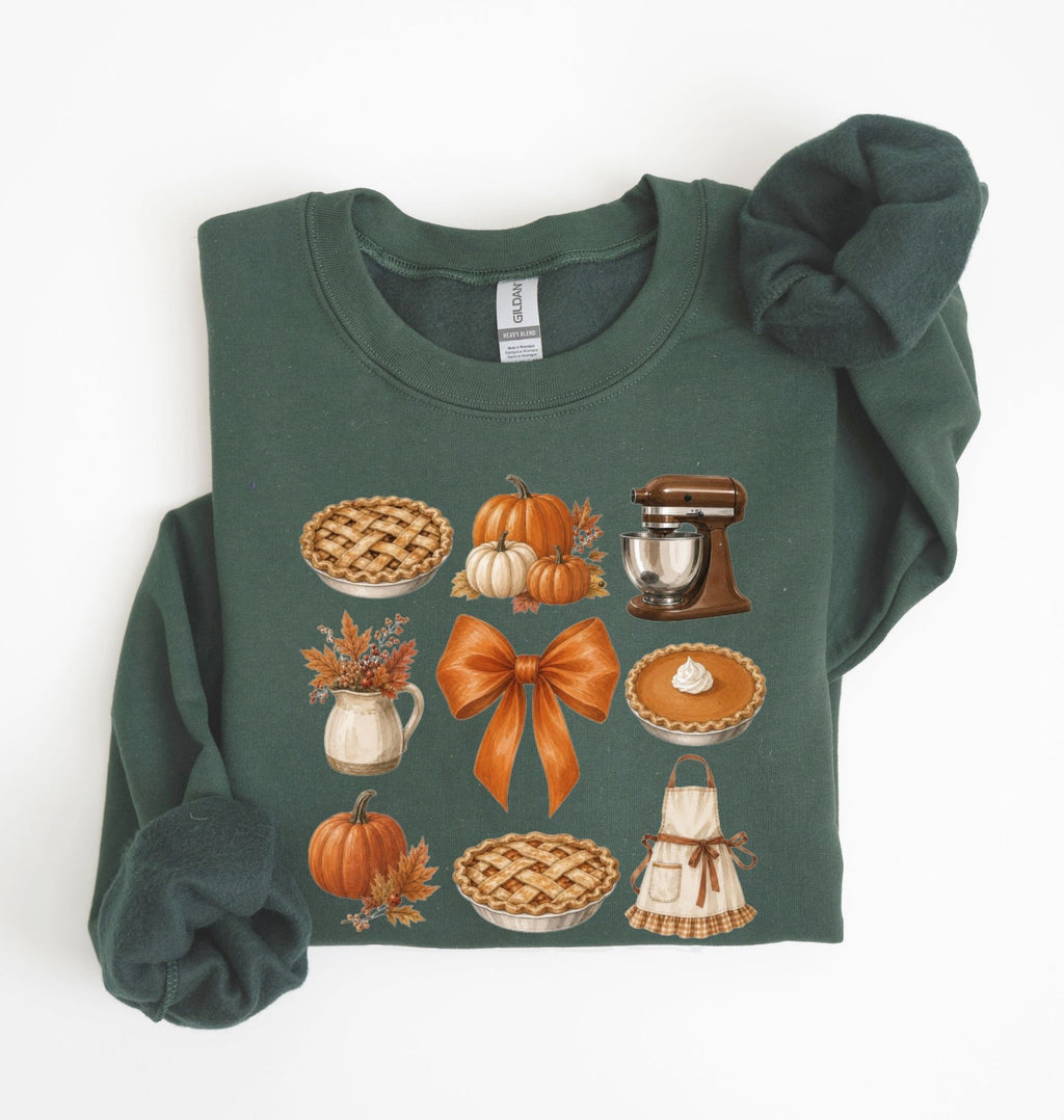 A dark green crewneck sweatshirt with long sleeves, featuring a graphic print of autumn-themed illustrations including pies, pumpkins, a stand mixer, and an orange bow. The sweatshirt is styled flat on a white background with the sleeves folded.