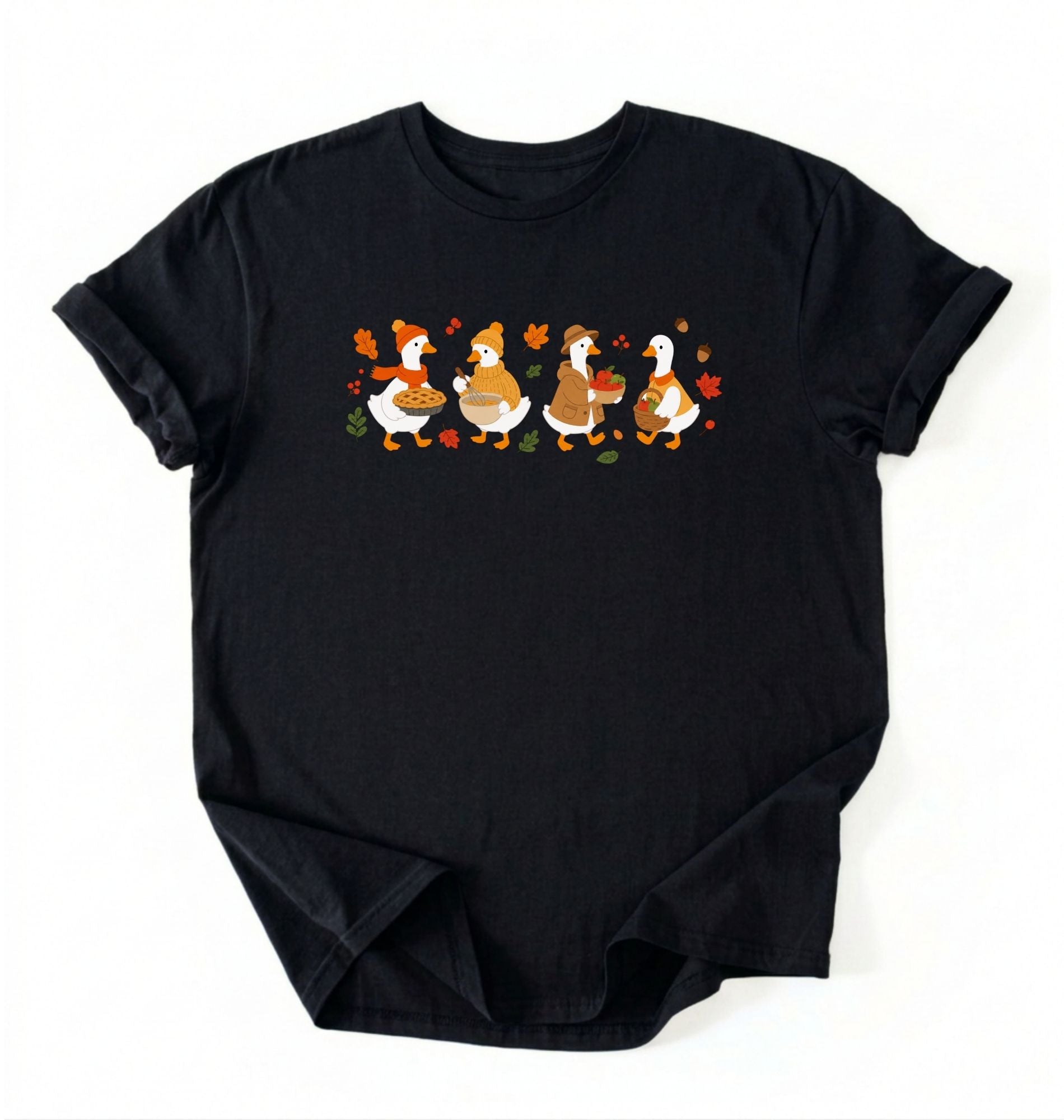 Flat lay of a black fall shirt featuring four geese baking pie, mixing ingredients and gathering apples on a white background 