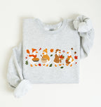 Flat lay of an ash fall sweatshirt featuring four geese baking pie, mixing ingredients and gathering apples on a white background