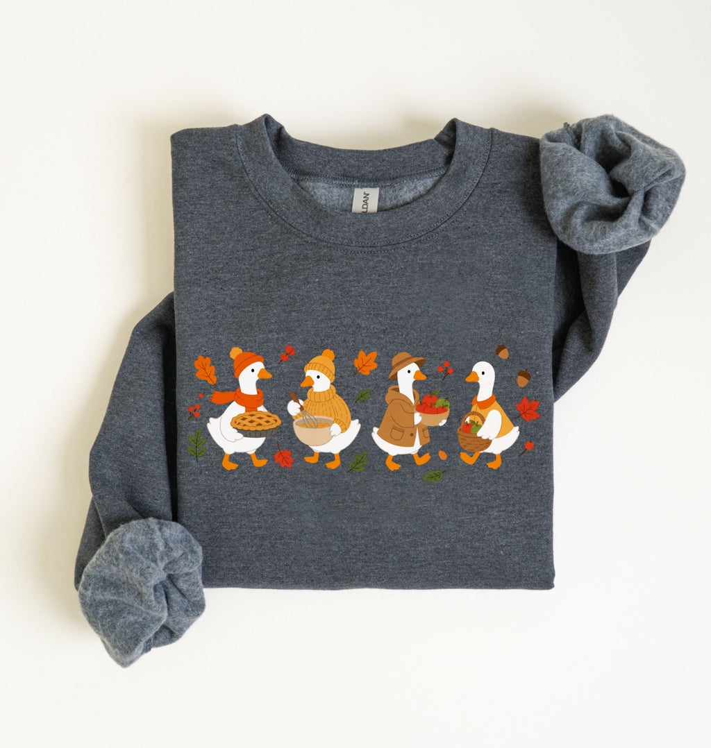 Flat lay of a dark heather fall sweatshirt featuring four geese baking pie, mixing ingredients and gathering apples on a white background