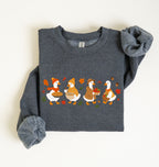 Flat lay of a dark heather fall sweatshirt featuring four geese baking pie, mixing ingredients and gathering apples on a white background
