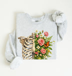 Flat lay of an Ash Floral ribcage sweatshirt with botanical flowers and butterfly, artistic skeleton plant lover gift on a white background