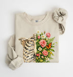 Flat lay of a Sand Floral ribcage sweatshirt with botanical flowers and butterfly, artistic skeleton plant lover gift on a white background