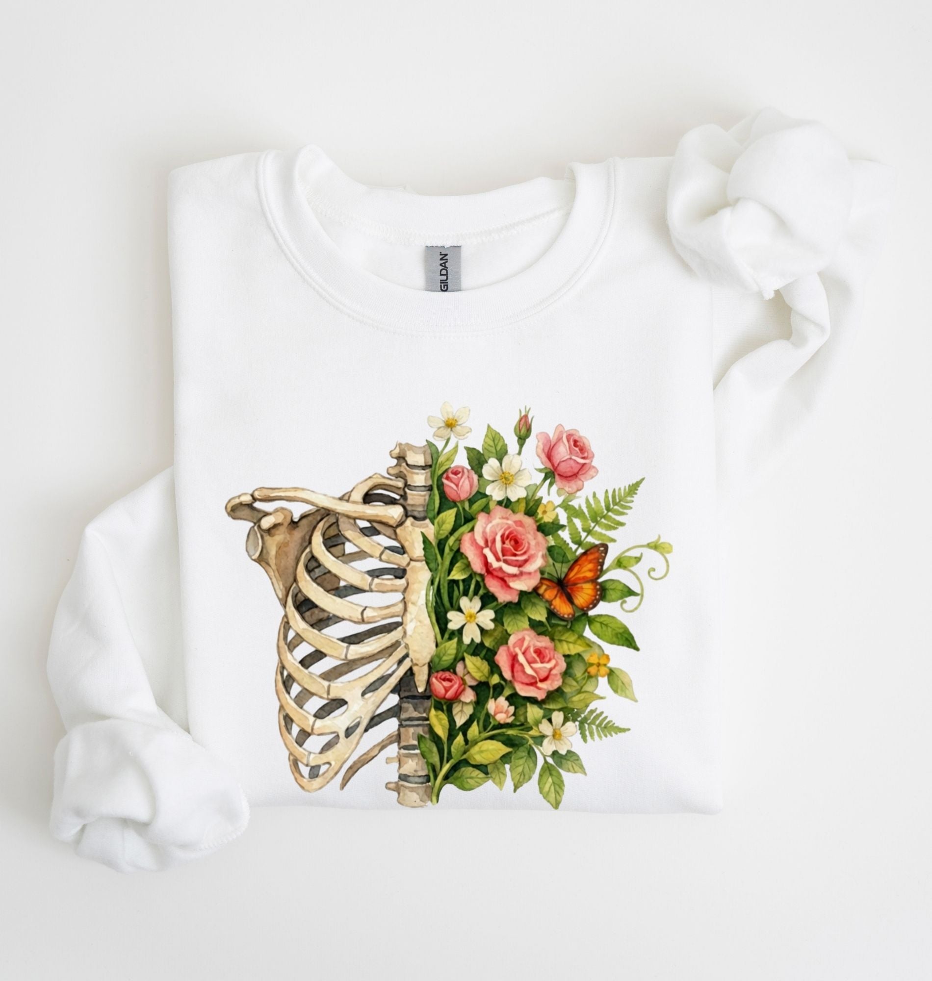 Flat lay of a White Floral ribcage sweatshirt with botanical flowers and butterfly, artistic skeleton plant lover gift on a white background