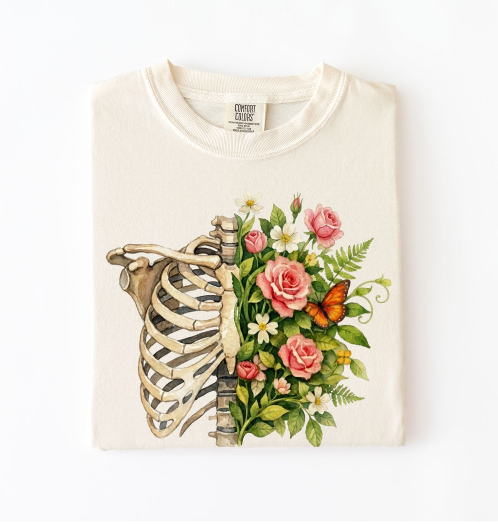 Flat lay of a Ivory Floral ribcage t-shirt with botanical flowers and butterfly, artistic skeleton plant lover gift on a white background