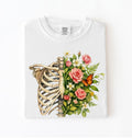 Flat lay of a White Floral ribcage t-shirt with botanical flowers and butterfly, artistic skeleton plant lover gift on a white background