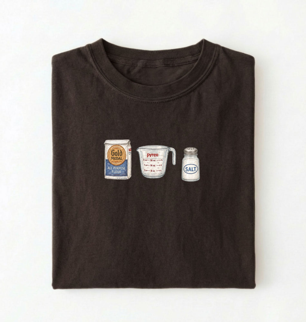 Flat lay of a brown flour water salt shirt with flour bag measuring cup and salt shaker minimalist bread baker gift on a white background 