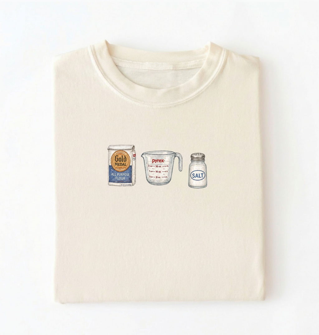 Flat lay of a cream flour water salt shirt with flour bag measuring cup and salt shaker minimalist bread baker gift on a white background 