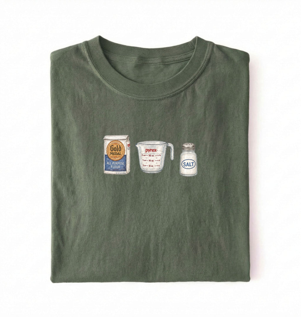Flat lay of a green flour water salt shirt with flour bag measuring cup and salt shaker minimalist bread baker gift on a white background 