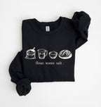 A black long-sleeve sweatshirt with rolled cuffs, featuring a white graphic of flour, water, and salt ingredients with the text 'flour. water.