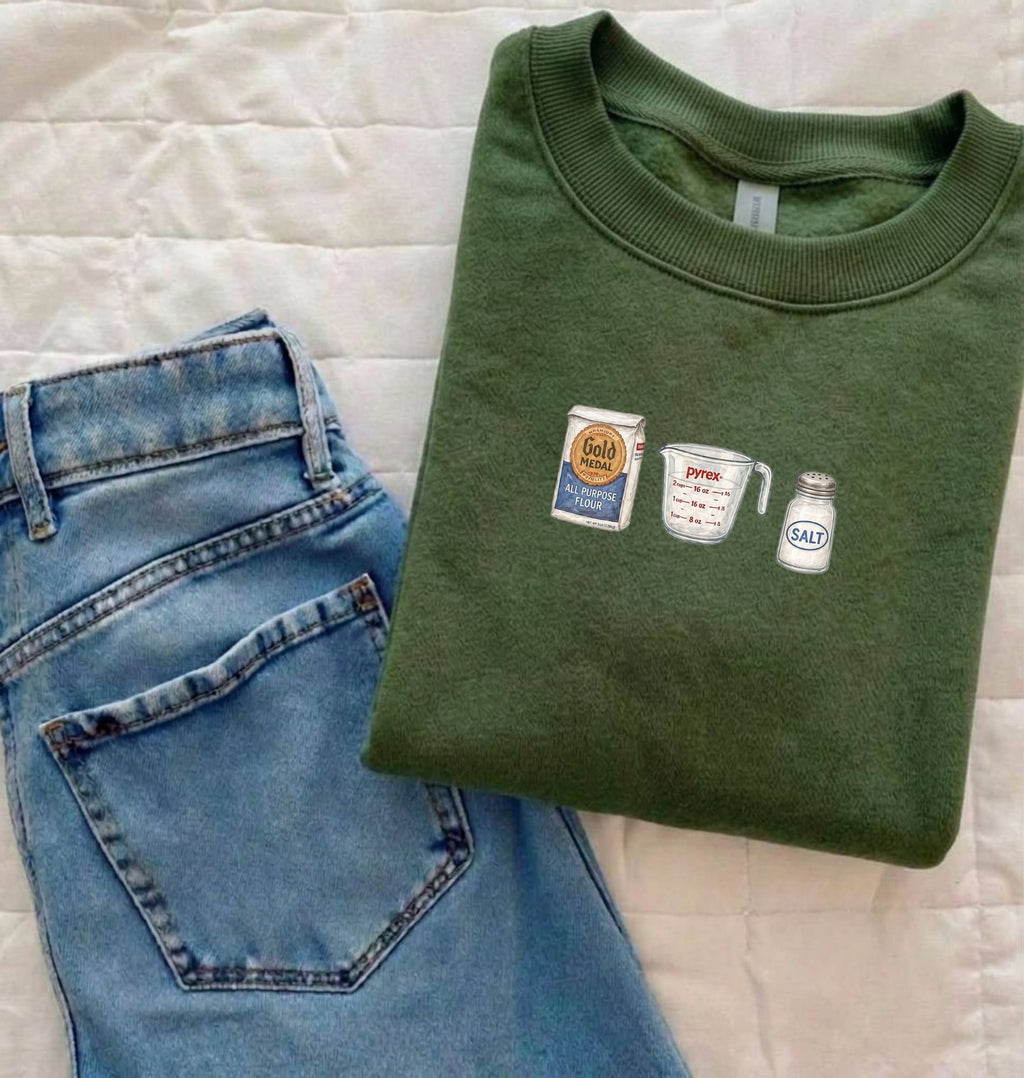 Flat lay of a green flour water salt sweatshirt with flour bag measuring cup and salt shaker for bread bakers 