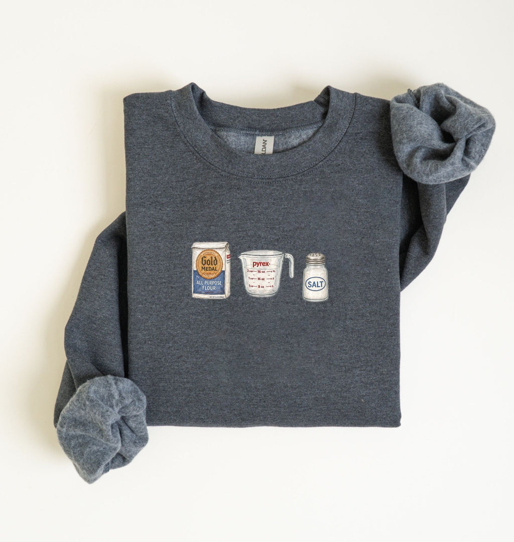 Flat lay of a dark heather flour water salt sweatshirt with flour bag measuring cup and salt shaker for bread bakers on a white background 