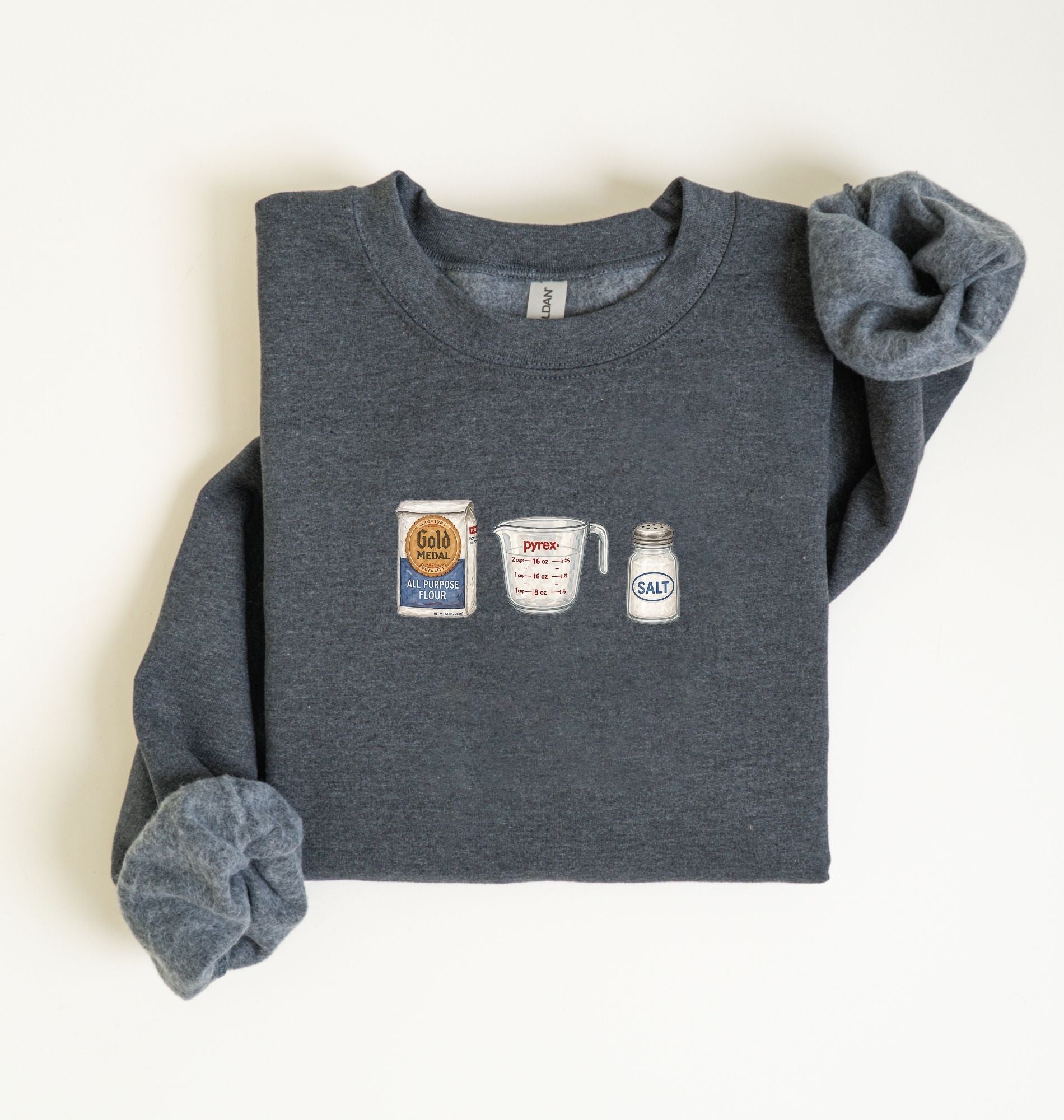 Flat lay of a dark heather flour water salt sweatshirt with flour bag measuring cup and salt shaker for bread bakers on a white background 