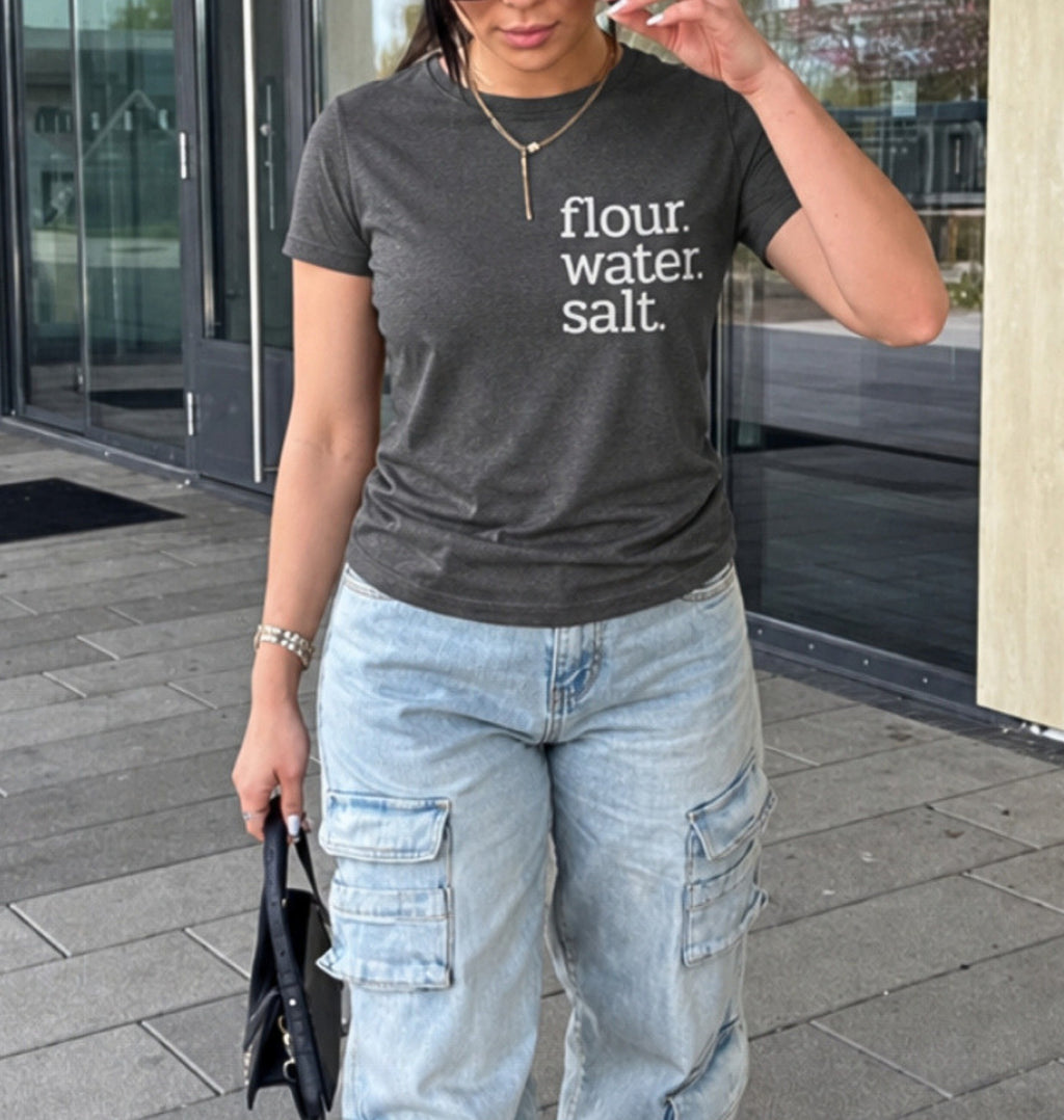 A woman wearing a dark gray heather t-shirt with the white text 'flour. water.