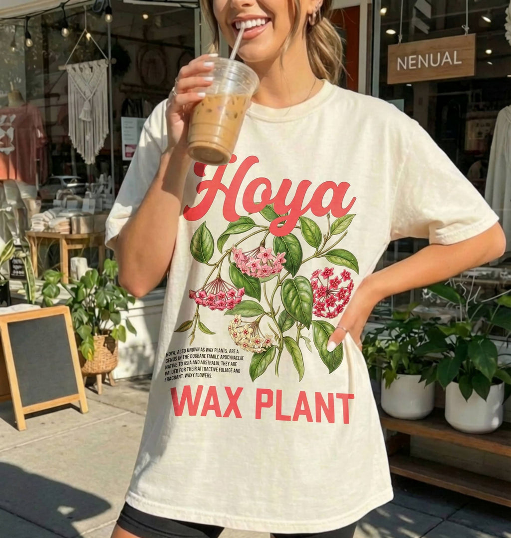 Person wearing a t-shirt with floral design and text, holding a drink outdoors.