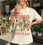 Person wearing a t-shirt with floral design and text, holding a drink outdoors.