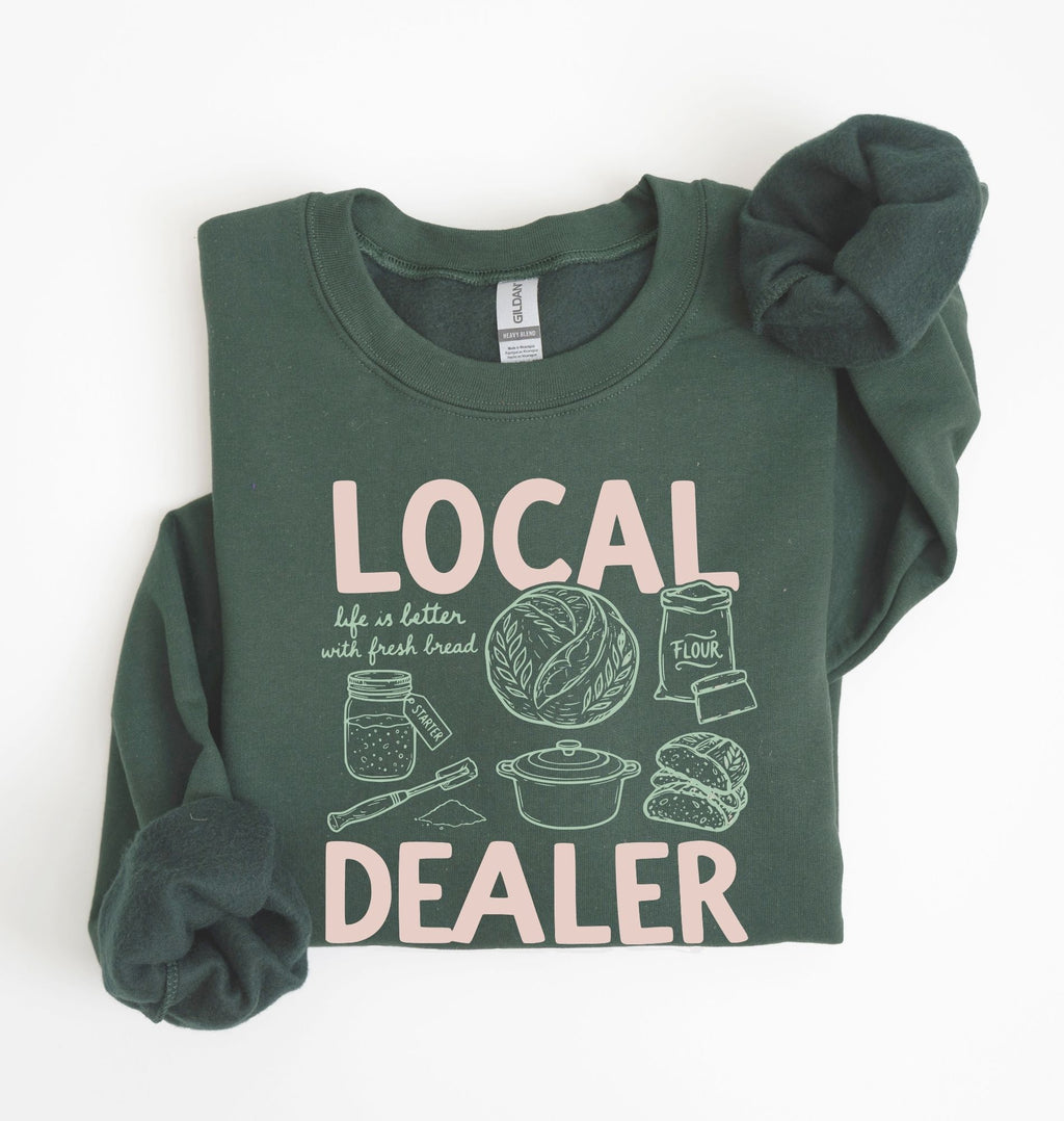Flat lay of an green cottagecore baking sweatshirt with Local Dealer text and bread graphics gift for bakers on a white background 