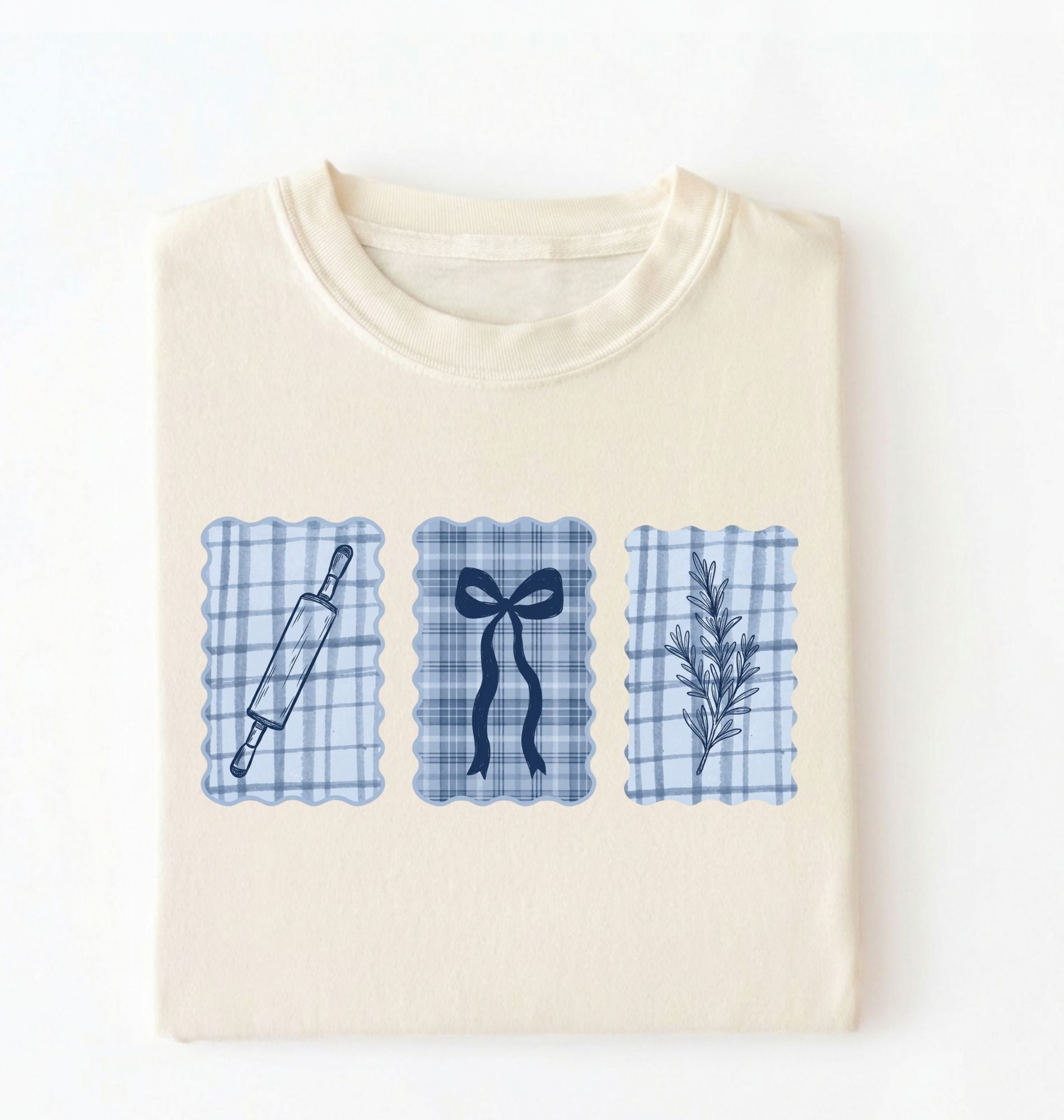 Flat lay of an ivory Cottagecore baking shirt with blue gingham pattern and baking icons perfect gift for bakers and vintage kitchen lovers on a white background 