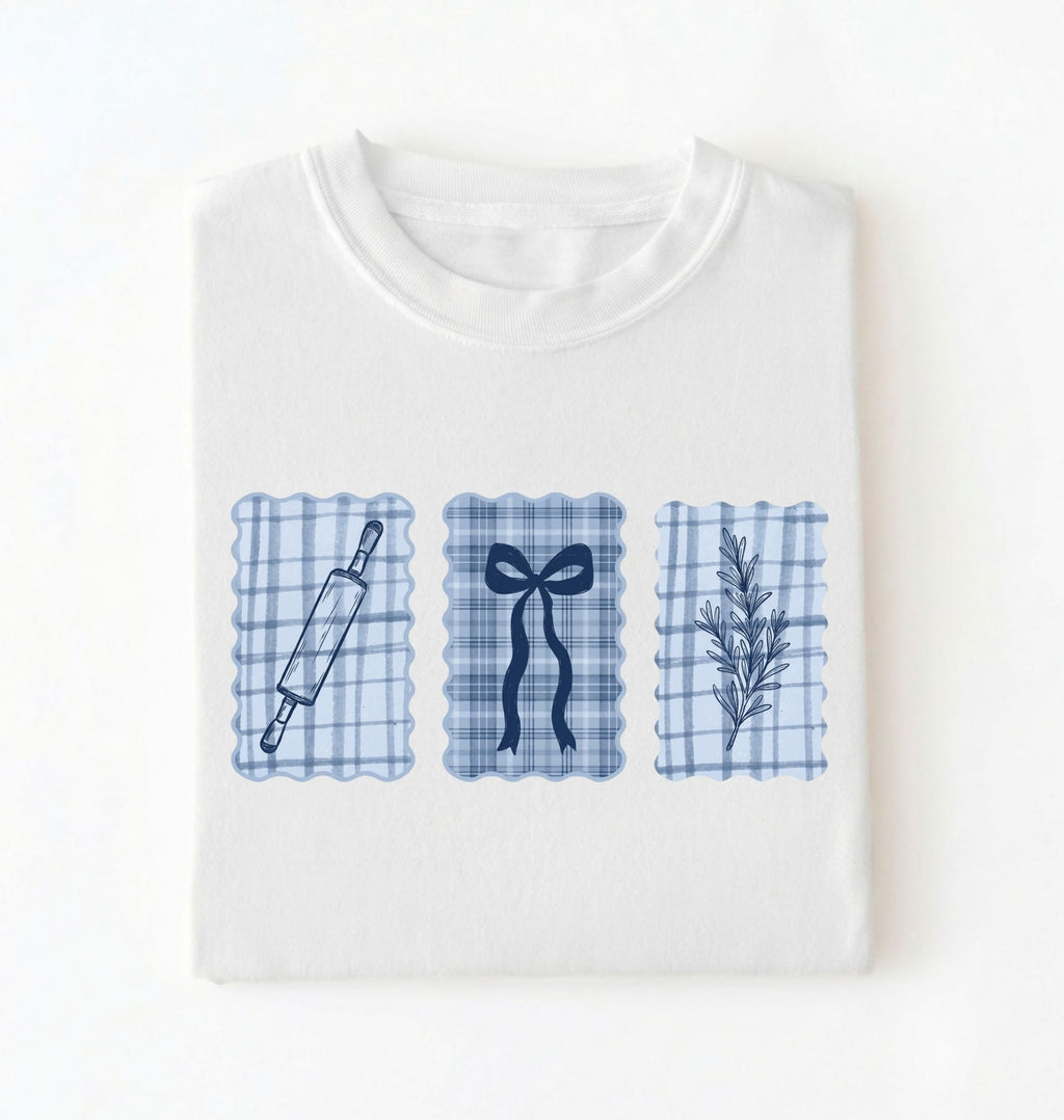 Flat lay of a white Cottagecore baking shirt with blue gingham pattern and baking icons perfect gift for bakers and vintage kitchen lovers on a white background 