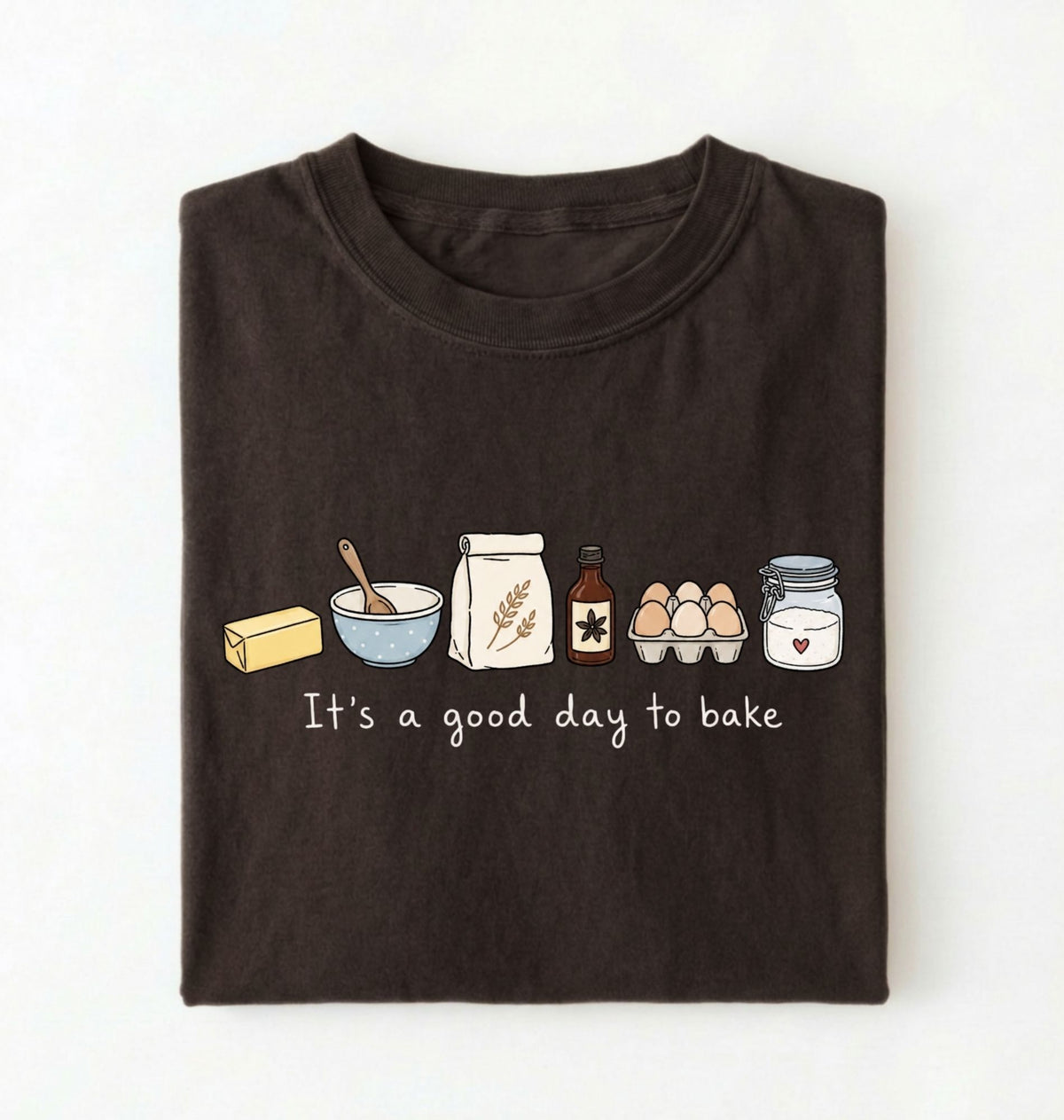 A dark brown folded t-shirt with a graphic of baking ingredients and the text 'It's a good day to bake' on a white background.
