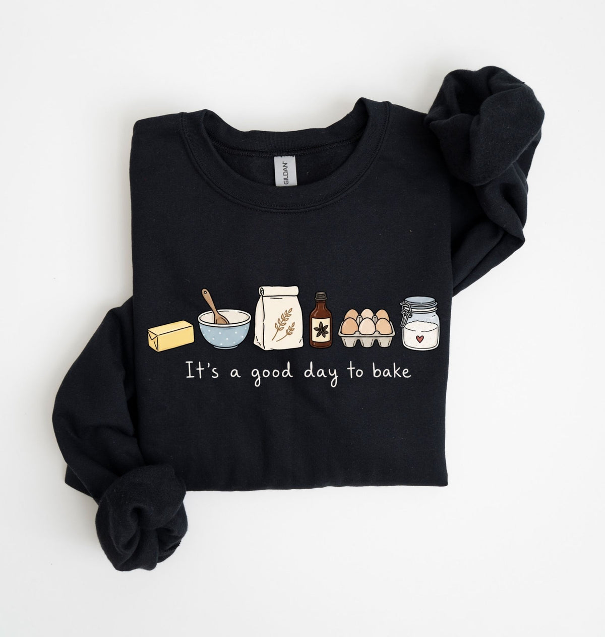 A black long-sleeve sweatshirt with rolled cuffs, featuring a cute baking-themed graphic on the chest with illustrations of a butter stick, bowl, spoon, flour sack, vanilla bottle, eggs, and jar above the text 'It's a good day to bake'.