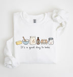 A white long-sleeve sweatshirt with a graphic of baking ingredients and the text 'It's a good day to bake' printed on the front, displayed on a clean white background.