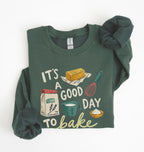 A dark green long-sleeve crewneck sweatshirt with a 'baking' themed graphic print, styled flat on a white background with the sleeves folded in.