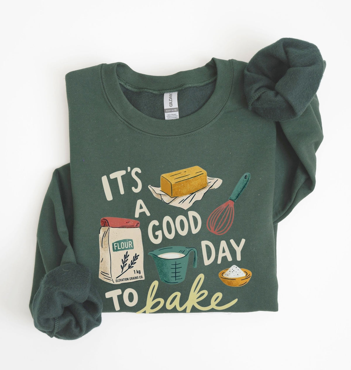 A dark green long-sleeve crewneck sweatshirt with a 'baking' themed graphic print, styled flat on a white background with the sleeves folded in.