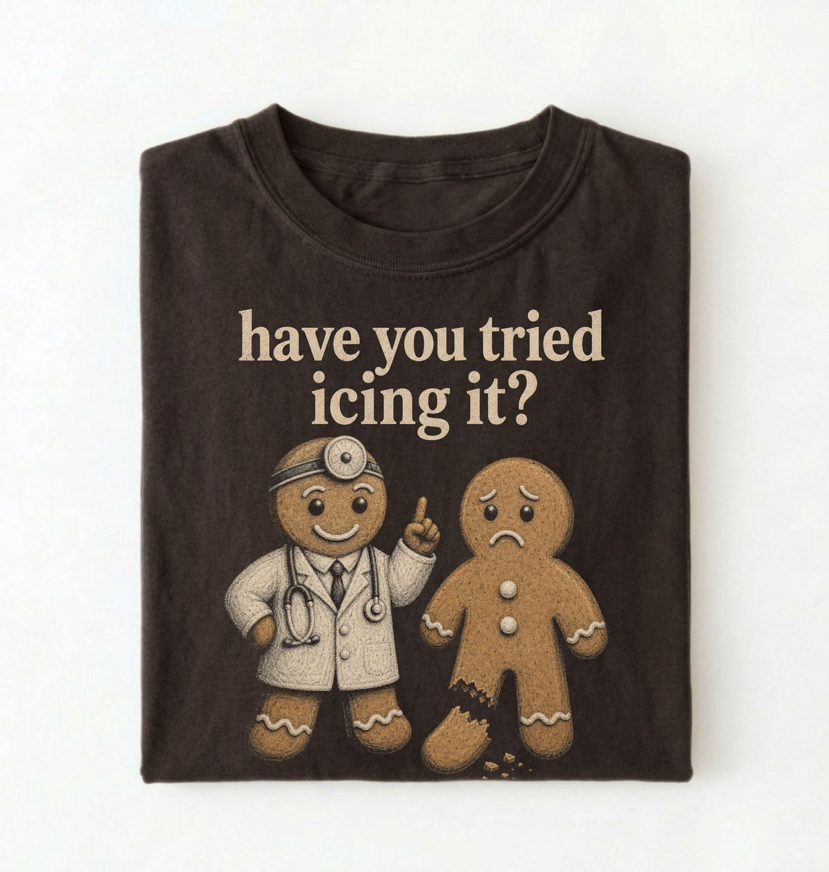 A folded dark brown t-shirt with a graphic print that reads 'have you tried icing it?' above two gingerbread figures, one dressed as a doctor and one sad gingerbread, on a white background.