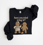 A black long-sleeve sweatshirt with a graphic print of two gingerbread men and the text 'have you tried icing it?' in beige, laid flat on a white background.