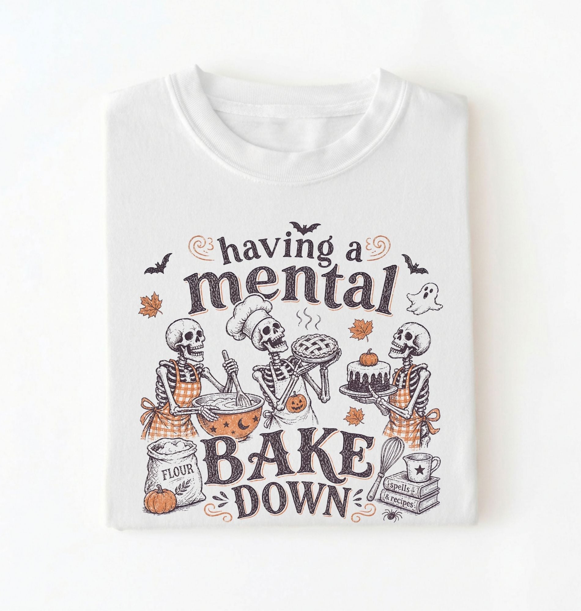 A white short-sleeve crewneck t-shirt featuring a Halloween-themed graphic print of three skeleton bakers with the text 'having a mental BAKE DOWN'. The graphic includes orange accents, bats, a ghost, and baking ingredients, shown on a clean white background.