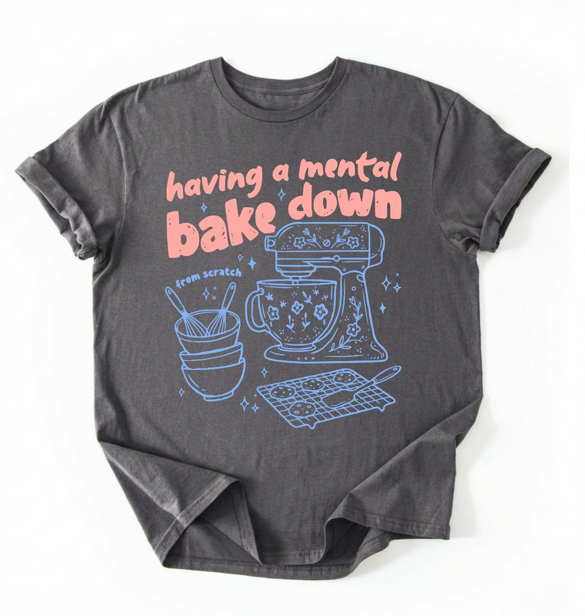 Flat lay of a Having a Mental Bake Down baking shirt with mixer graphic on brown t-shirt on a ivory background