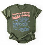 Flat lay of a Having a Mental Bake Down baking shirt with mixer graphic on black t-shirt on a green background