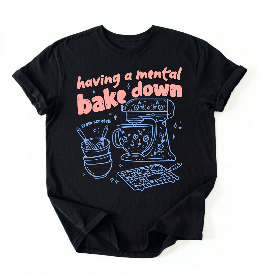 Flat lay of a Having a Mental Bake Down baking shirt with mixer graphic on black t-shirt on a ivory background