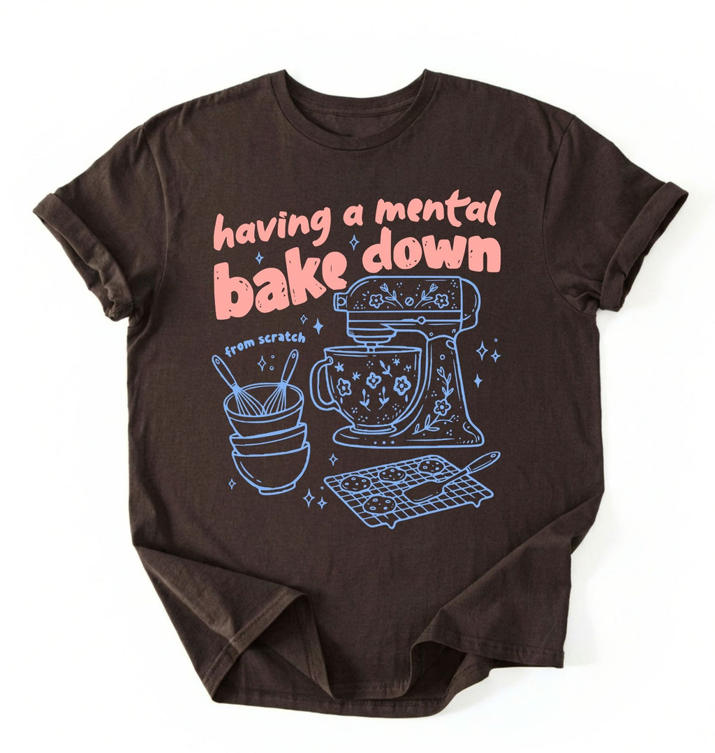 Flat lay of a Having a Mental Bake Down baking shirt with mixer graphic on brown t-shirt on a white background