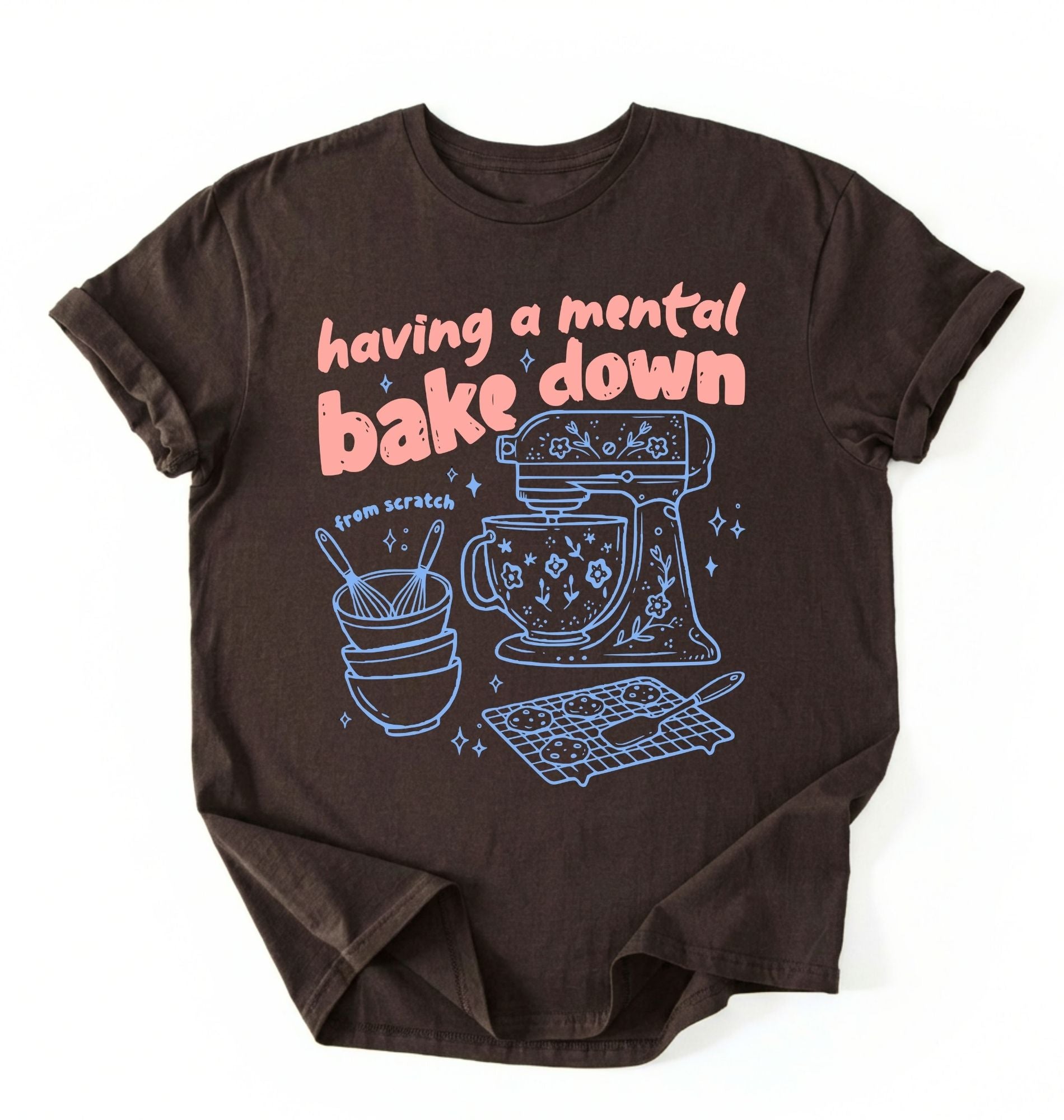 Flat lay of a Having a Mental Bake Down baking shirt with mixer graphic on brown t-shirt on a white background