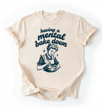 Flat lay of a cream having a mental bake down shirt with vintage baker illustration funny baking lover gift on a white background 