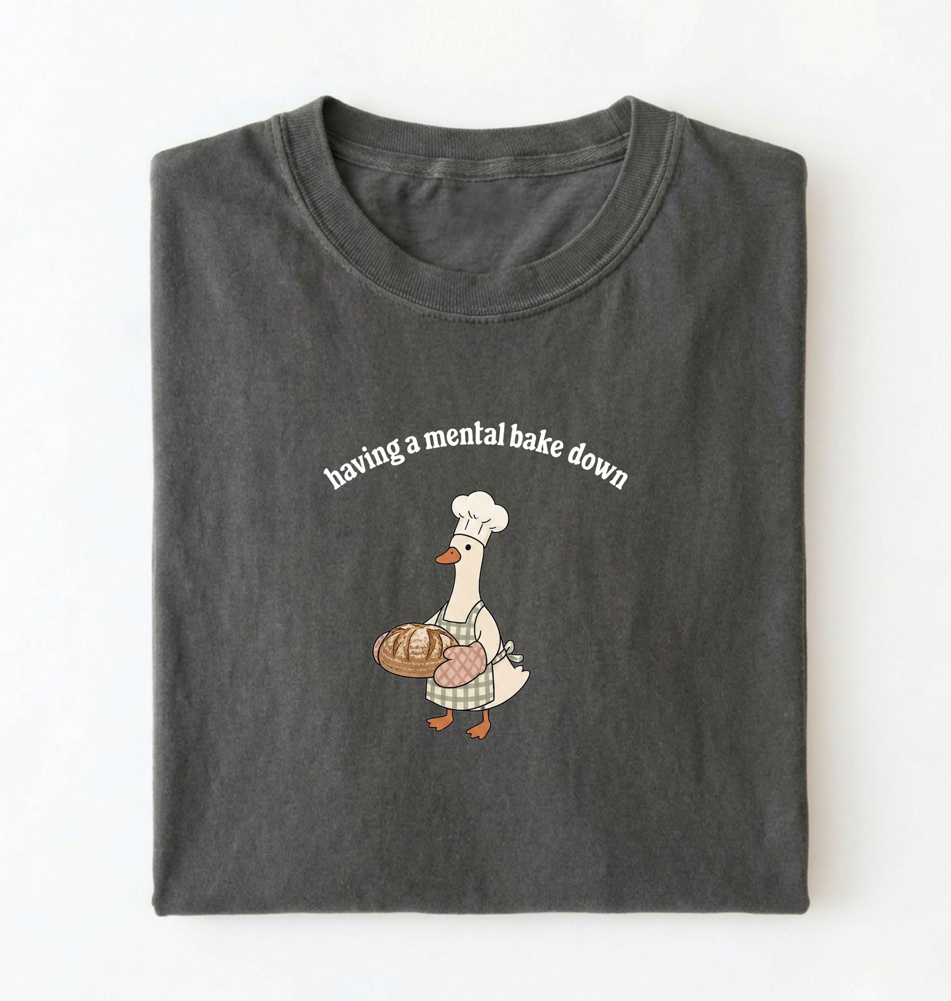 Flat lay of a gray Funny Having a Mental Bake Down shirt with baker goose holding artisan bread graphic on a white background 