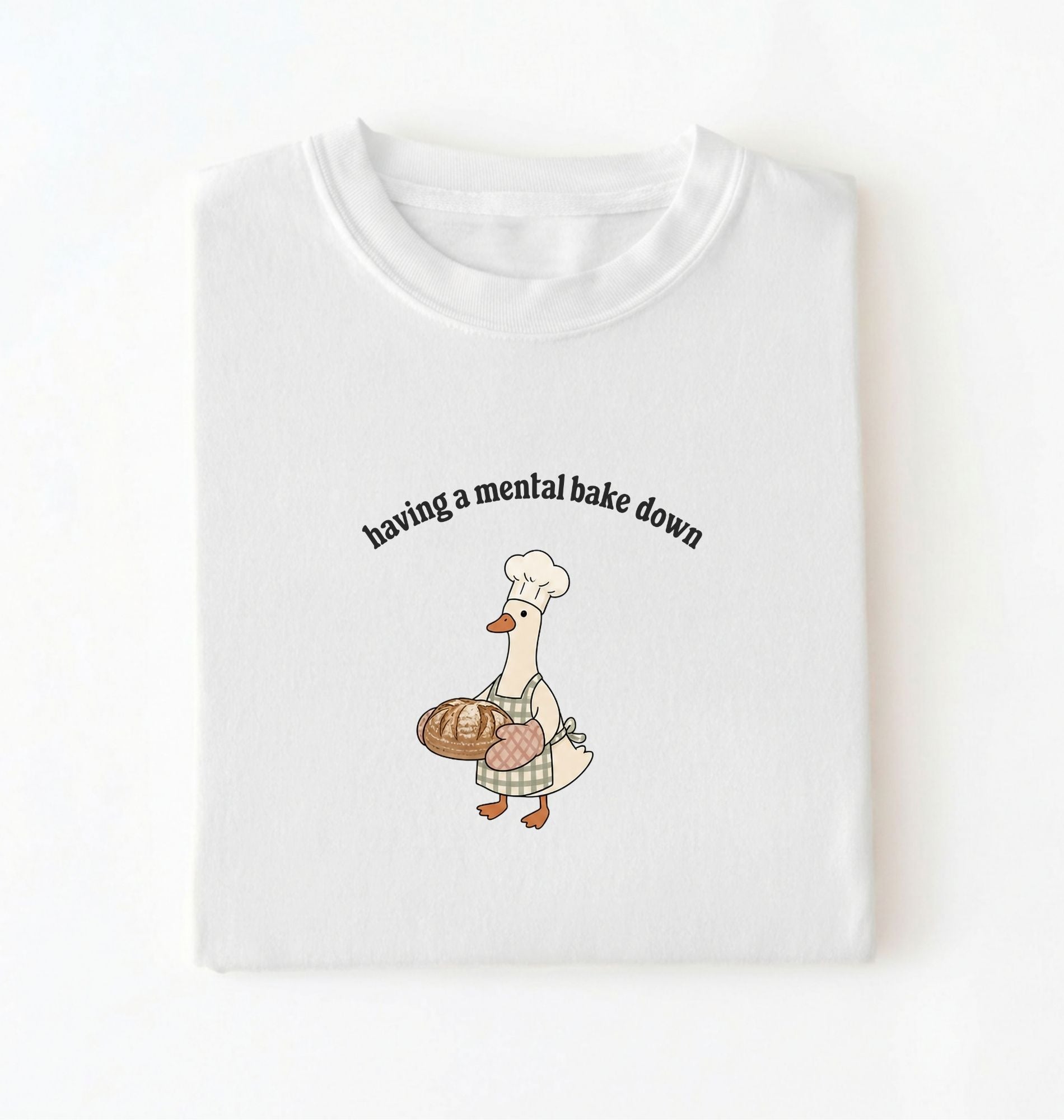 Flat lay of a white Funny Having a Mental Bake Down shirt with baker goose holding artisan bread graphic on a white background 