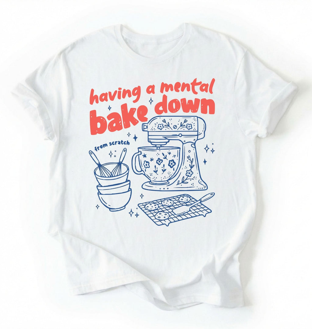 Flat lay of a Having a Mental Bake Down baking shirt with mixer graphic on white t-shirt on a ivory background